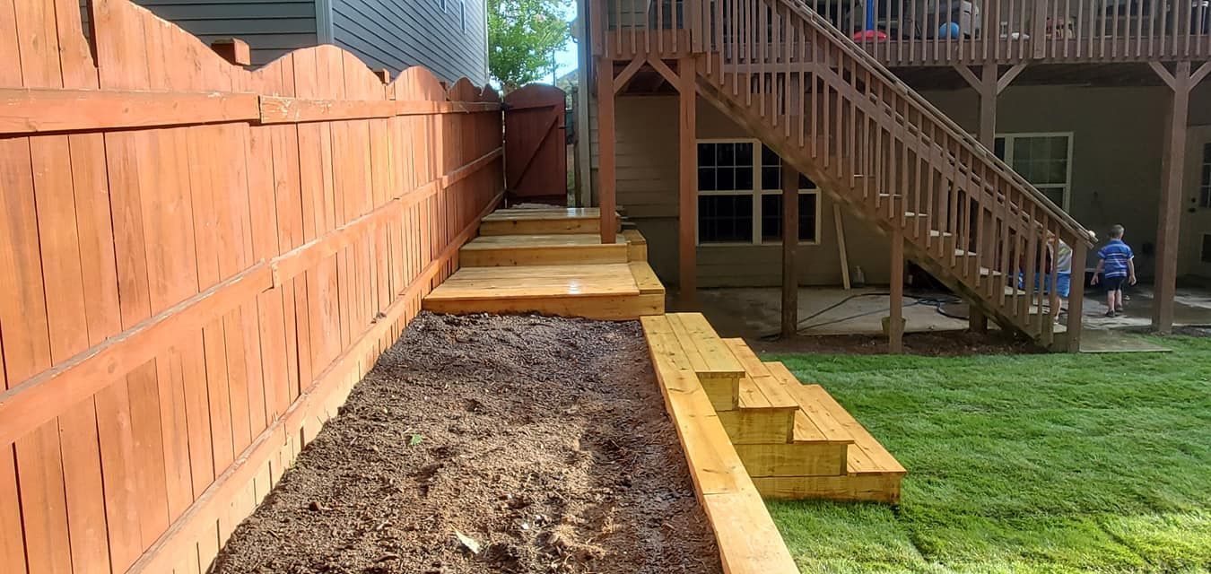 Backyard garden bed with wooden edging beside a deck, stairs, and a retaining wall