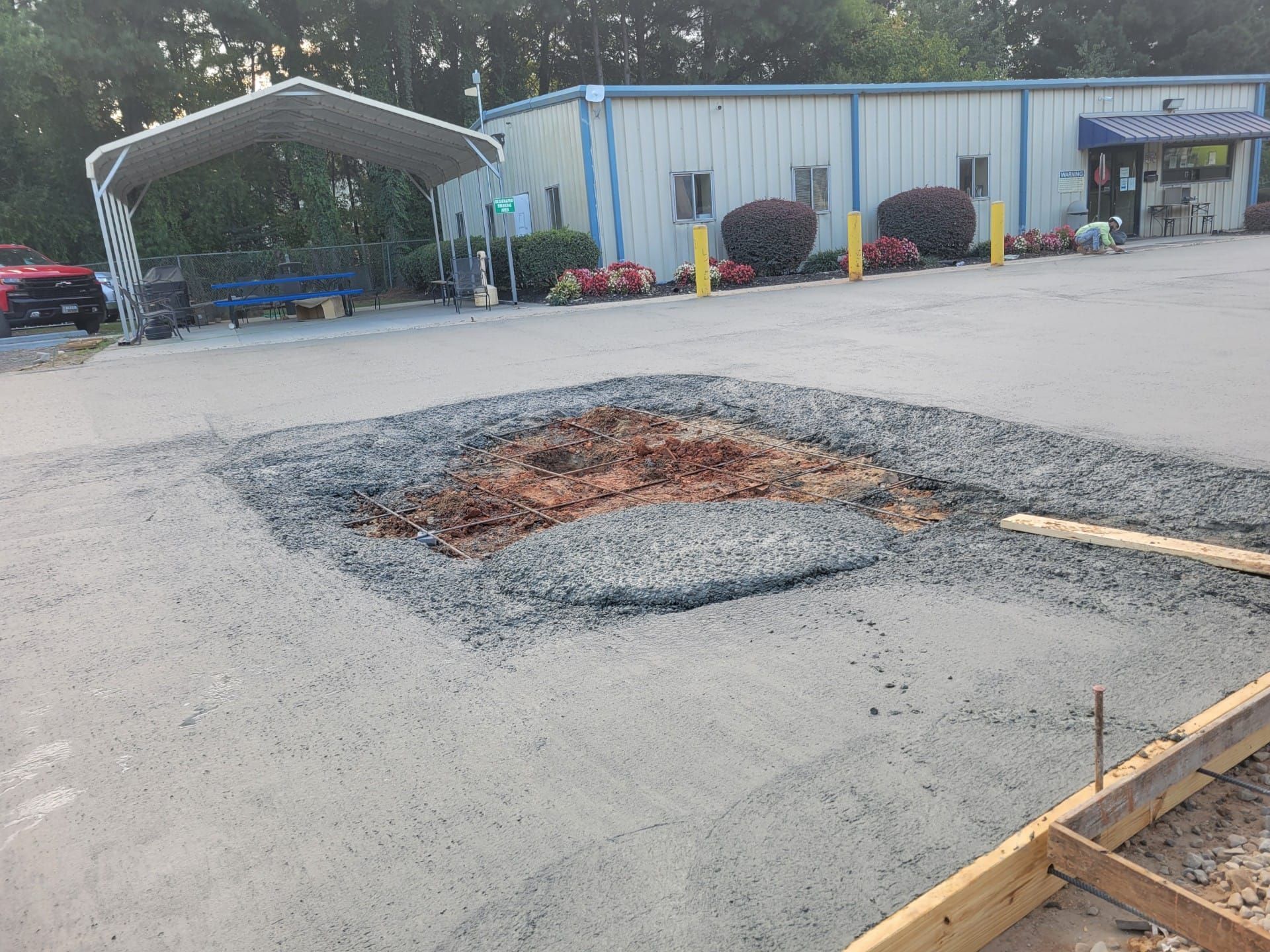 Pothole patch in an asphalt parking lot outside a metal building, with gravel and construction materials nearby
