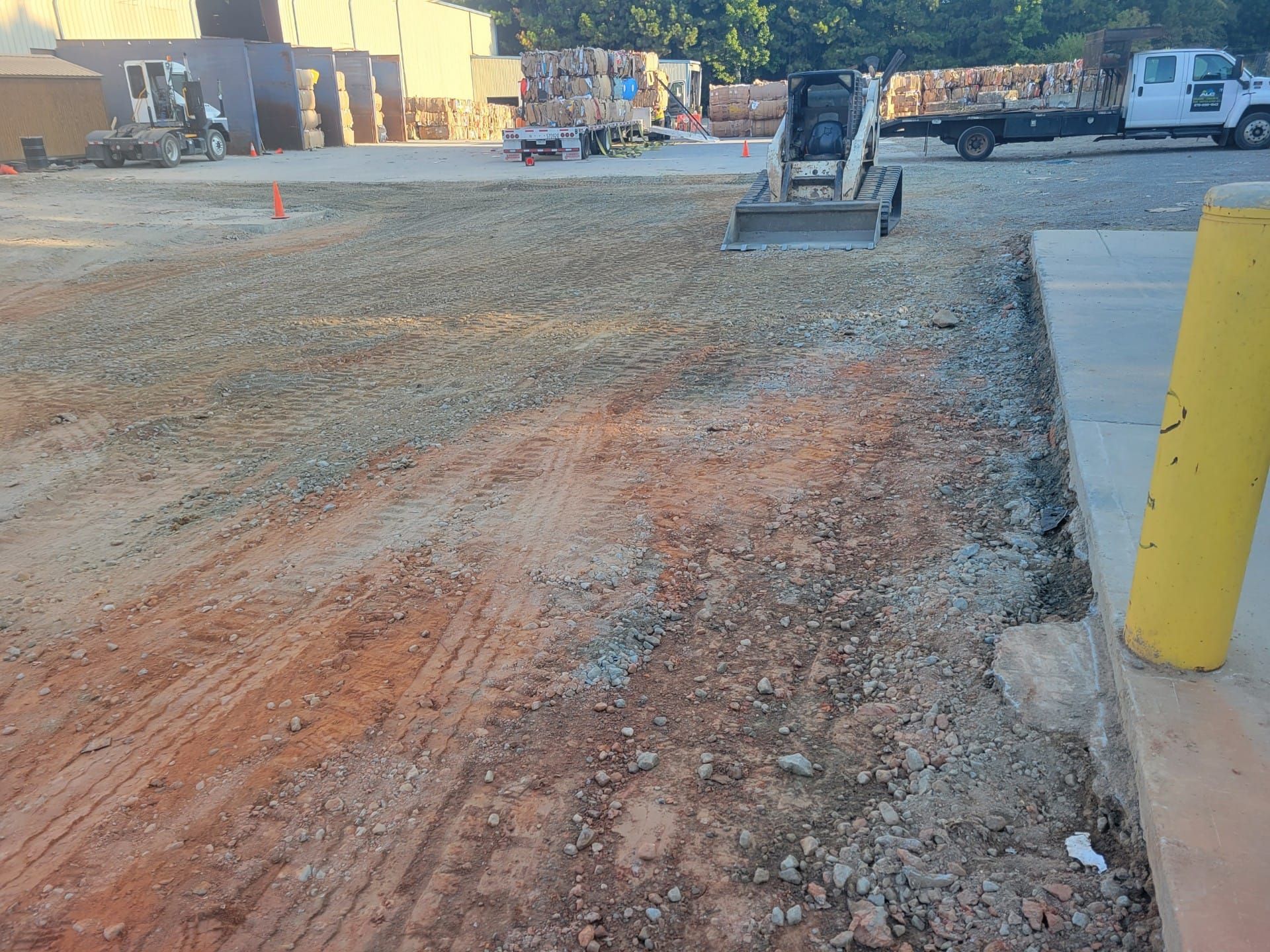 Construction site with gravel roadbed, an excavator in the distance, and yellow bollards on the right.