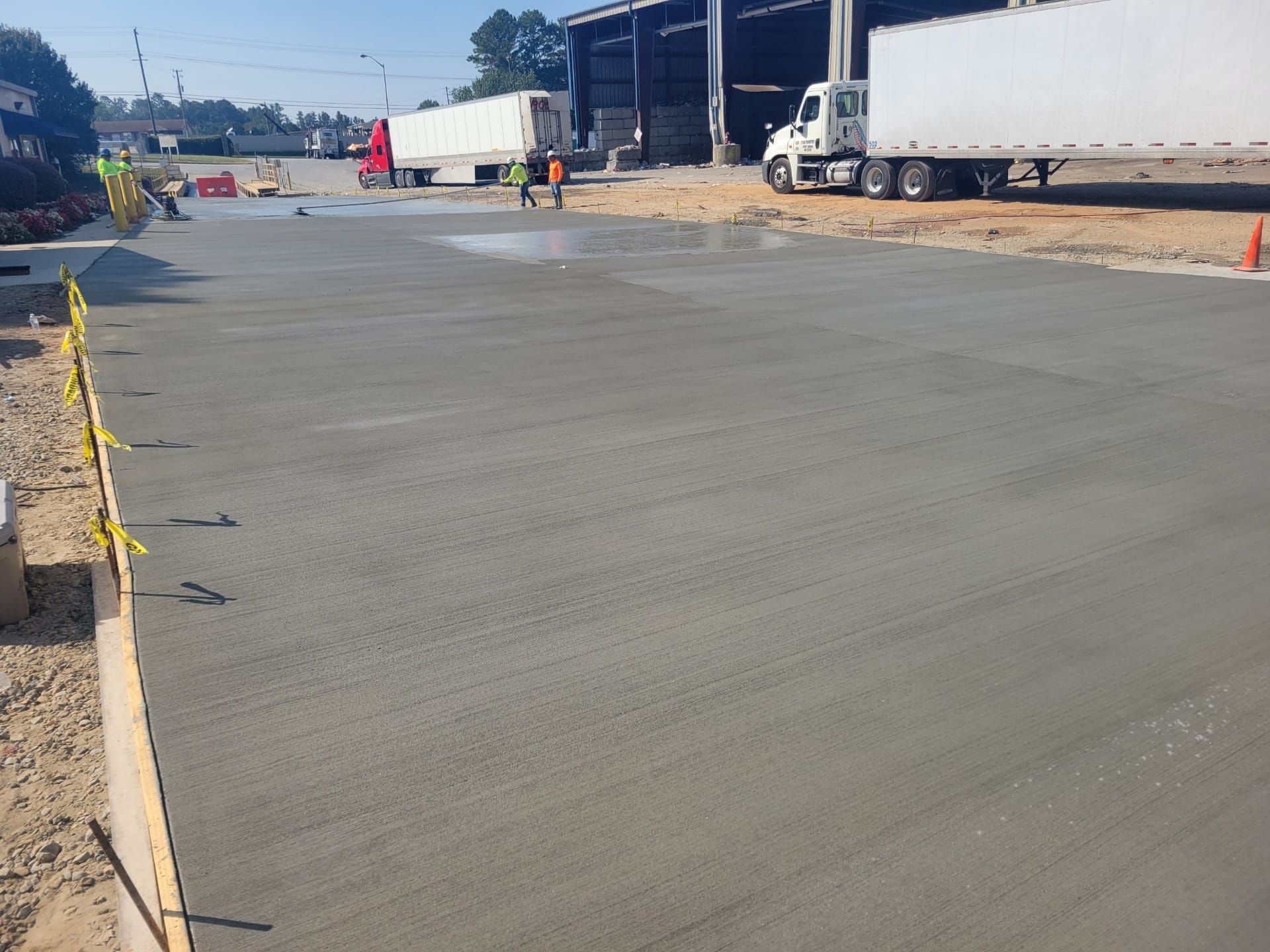 Paved industrial yard with trucks, workers, and traffic cones under a clear blue sky