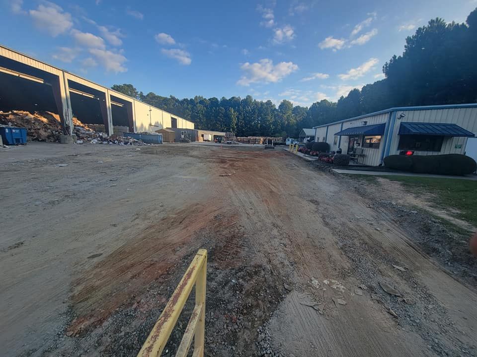 Wide dirt lot between industrial buildings at sunset, with trucks and equipment along the sides.