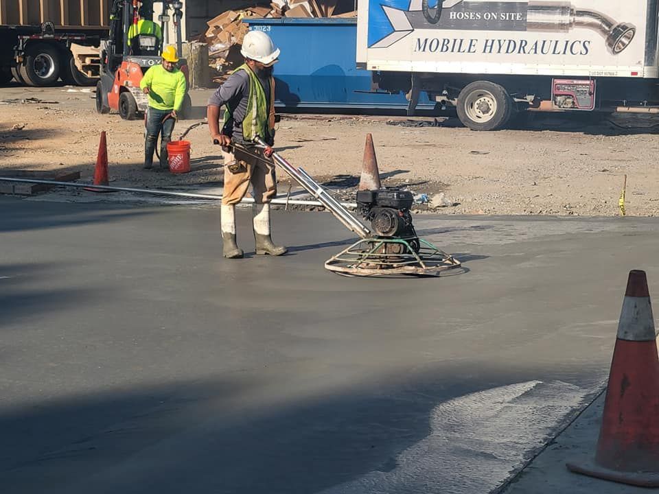 Workers operating a pavement grinder on a road construction site with cones and equipment nearby