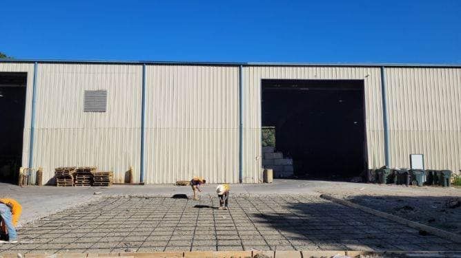 Industrial warehouse exterior with open loading bay and paved foreground under bright daylight