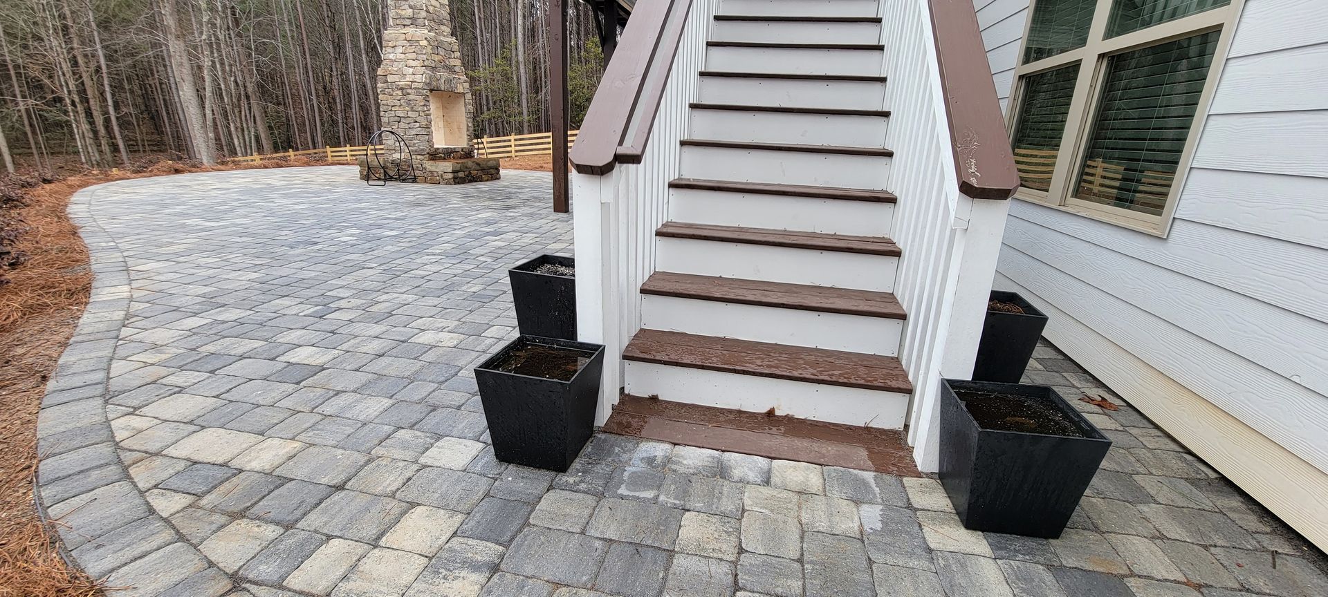 Stone-paver walkway to front steps and porch of a white house, with two black planters by the stairs