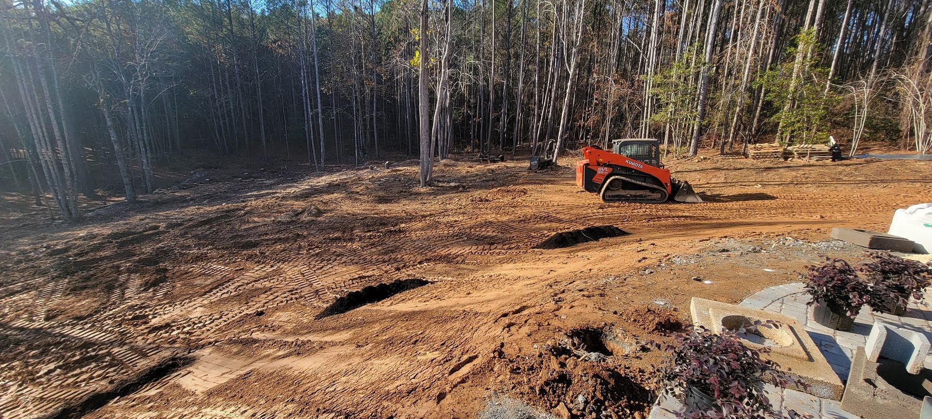 Small orange excavator on a cleared dirt lot with trees in the background