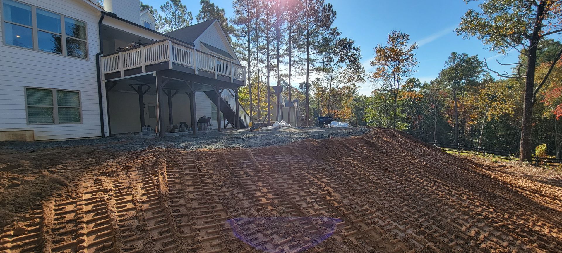 House with deck above a freshly graded dirt yard under sunny autumn trees