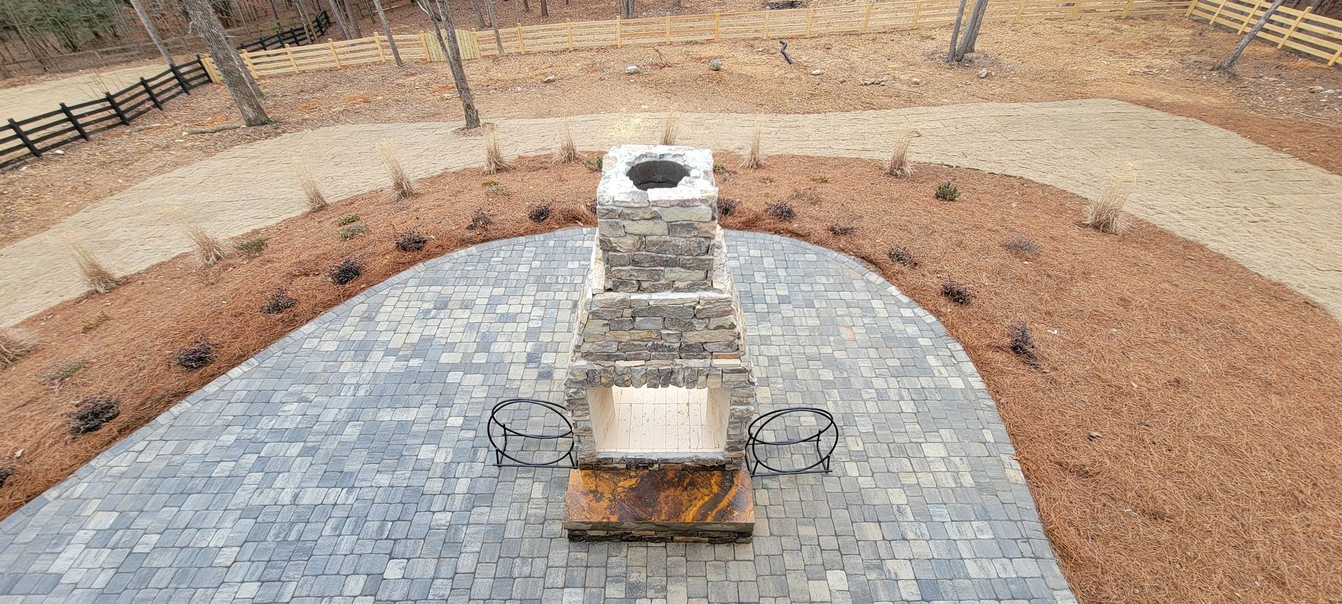Stone monument on a paved platform in a park with mulch and grass surrounds