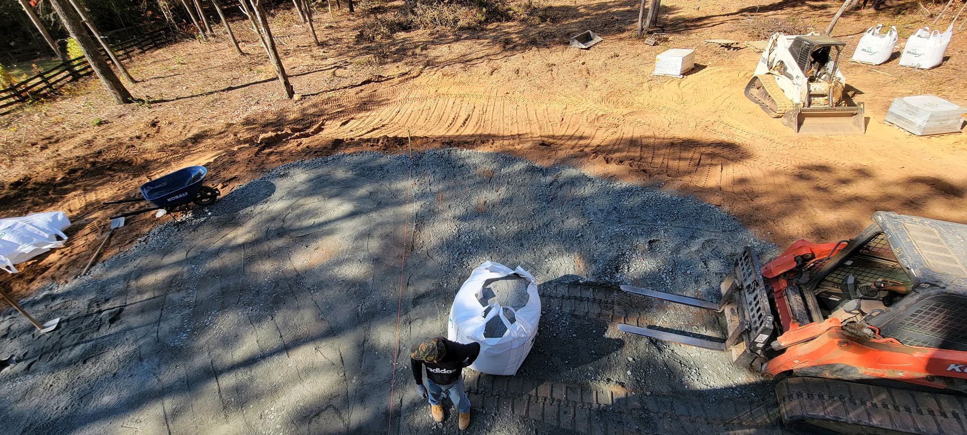 Aerial view of a yard with a black tarp, a person in white crouching, and an orange tractor on the right