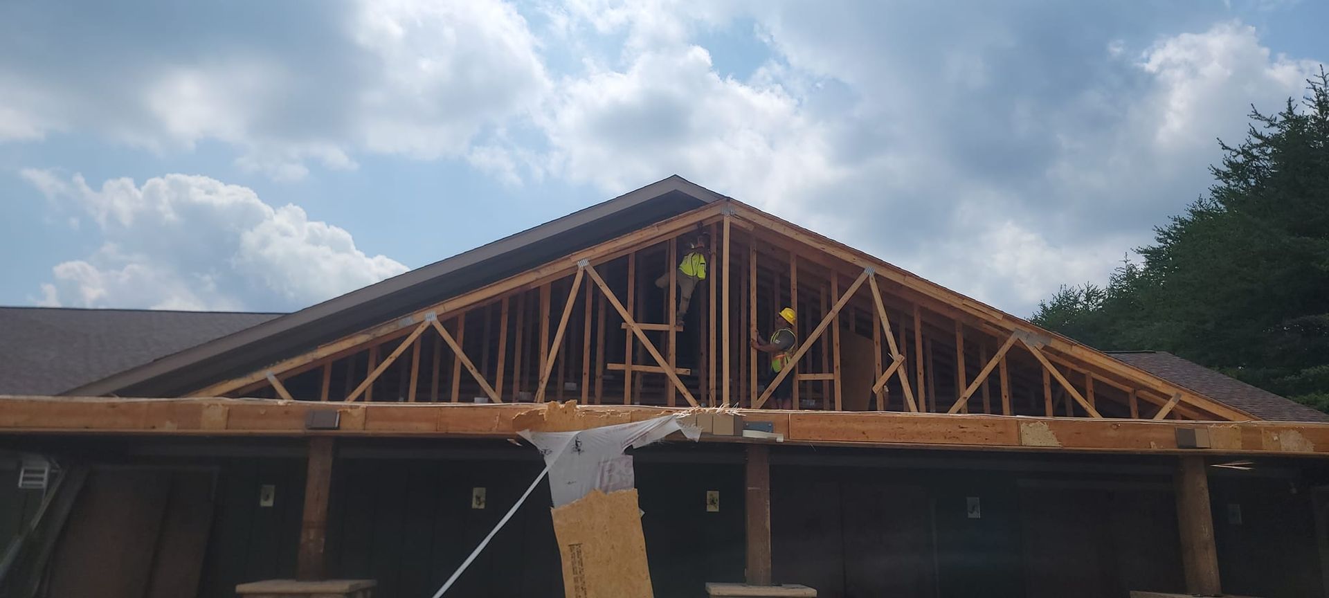 Exterior of a wooden building under construction with exposed roof trusses and brick columns