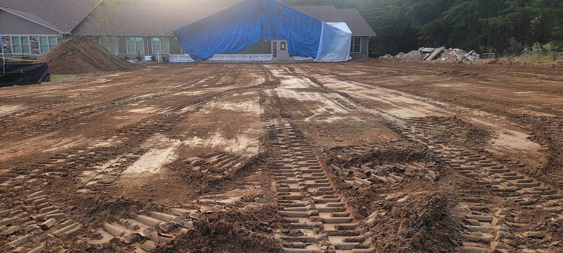 Muddy construction site with tire tracks and blue tarps covering structures in the background