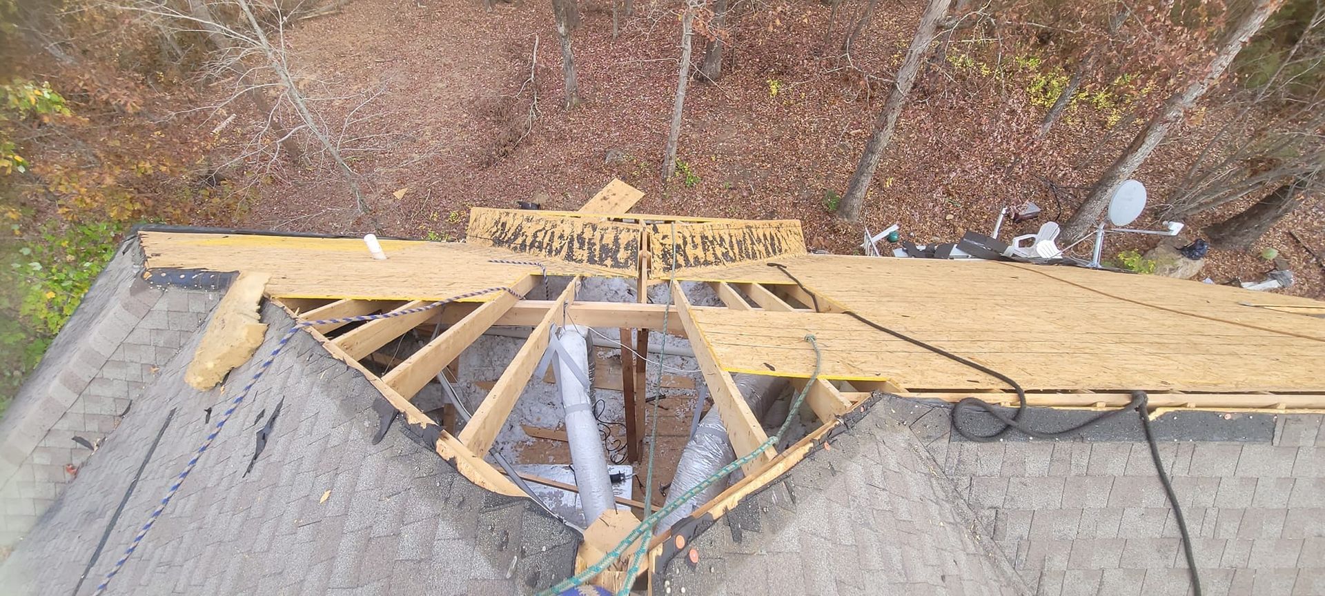 Damaged rooftop with a large hole exposing wooden framing and debris beside an orange chair.