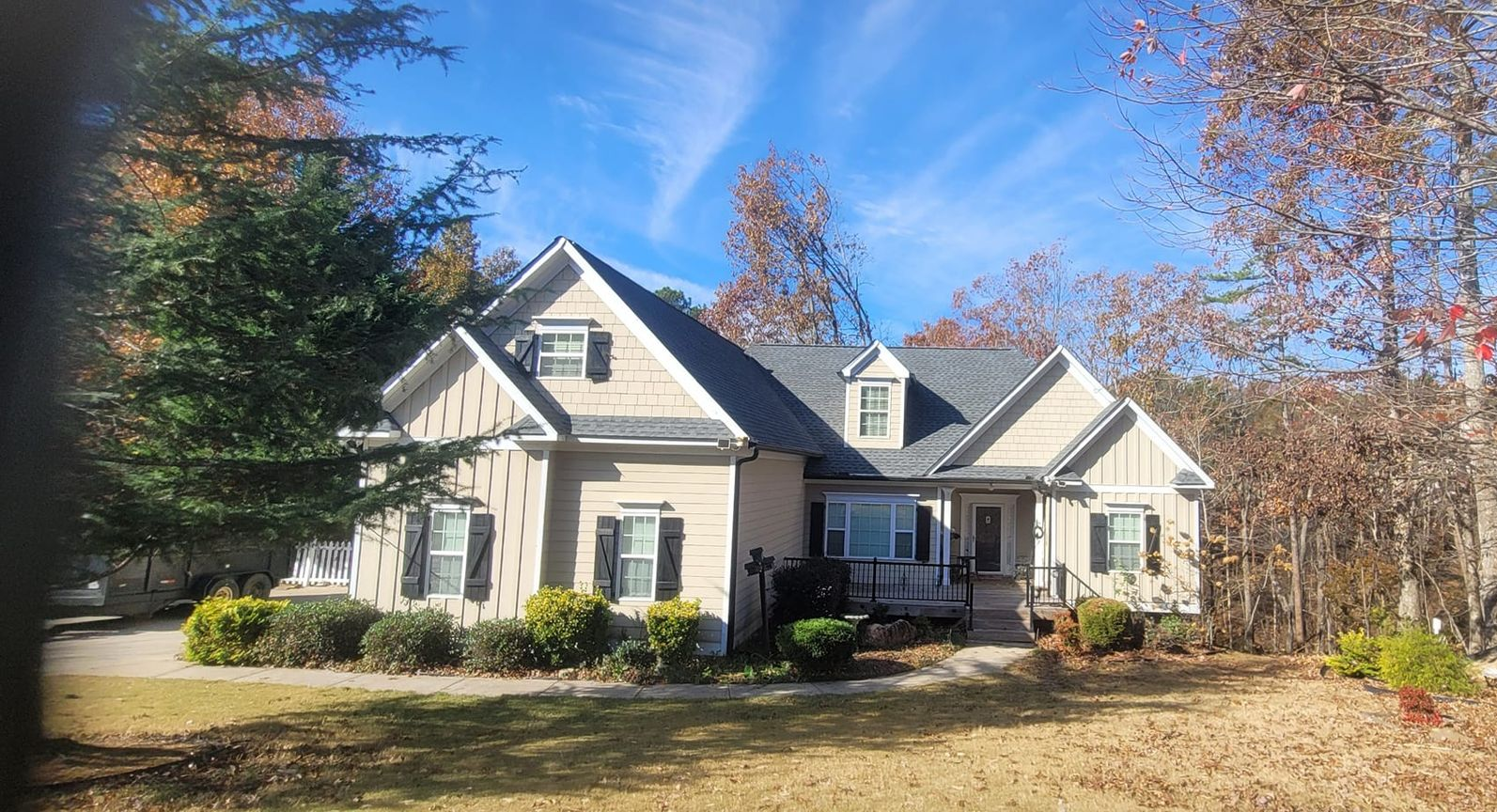 Suburban house with beige siding, dark roof, and front porch surrounded by trees in autumn.