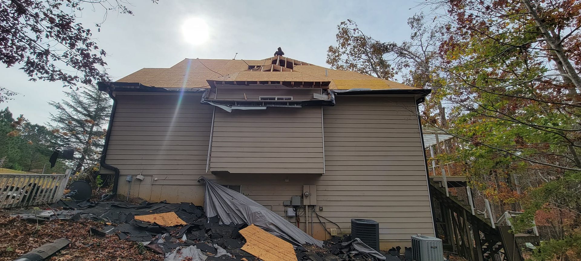 Severely damaged house with a collapsed roof and debris in front, surrounded by trees.