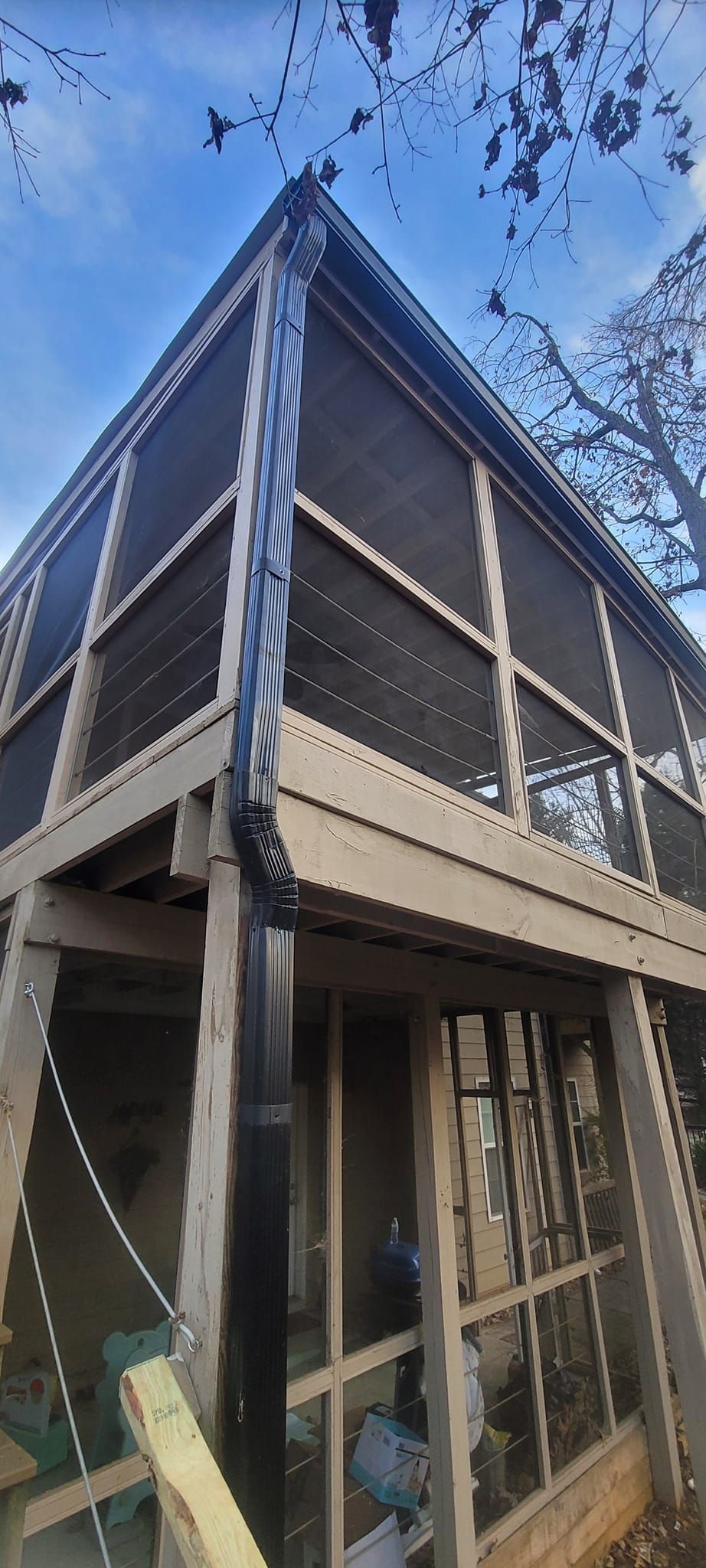 Tall wooden house under construction with exposed framing and blue sky above