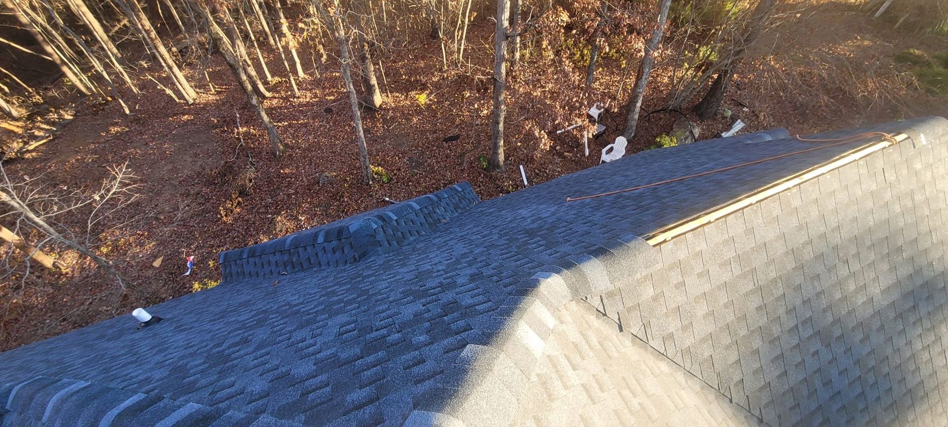 Roof shingles at the edge of a roof, overlooking trees and brown ground below