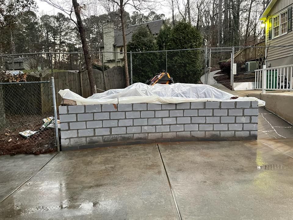 Person lying under a white tarp on a cinder block platform in a wet backyard construction area