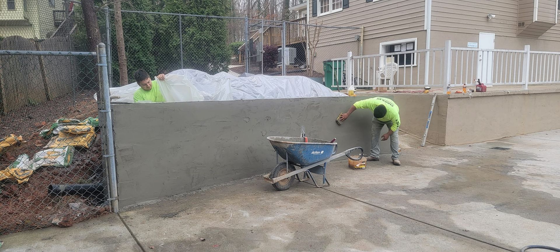 Worker smoothing concrete beside a wheelbarrow at an outdoor construction site