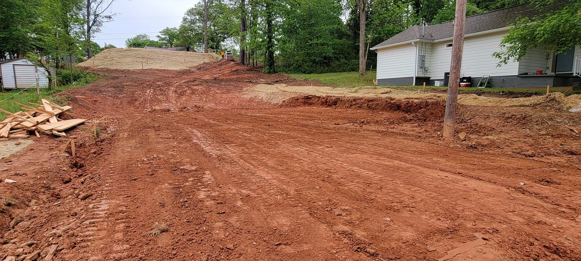 Freshly graded red dirt driveway leading to a house with trees and a utility pole on the right