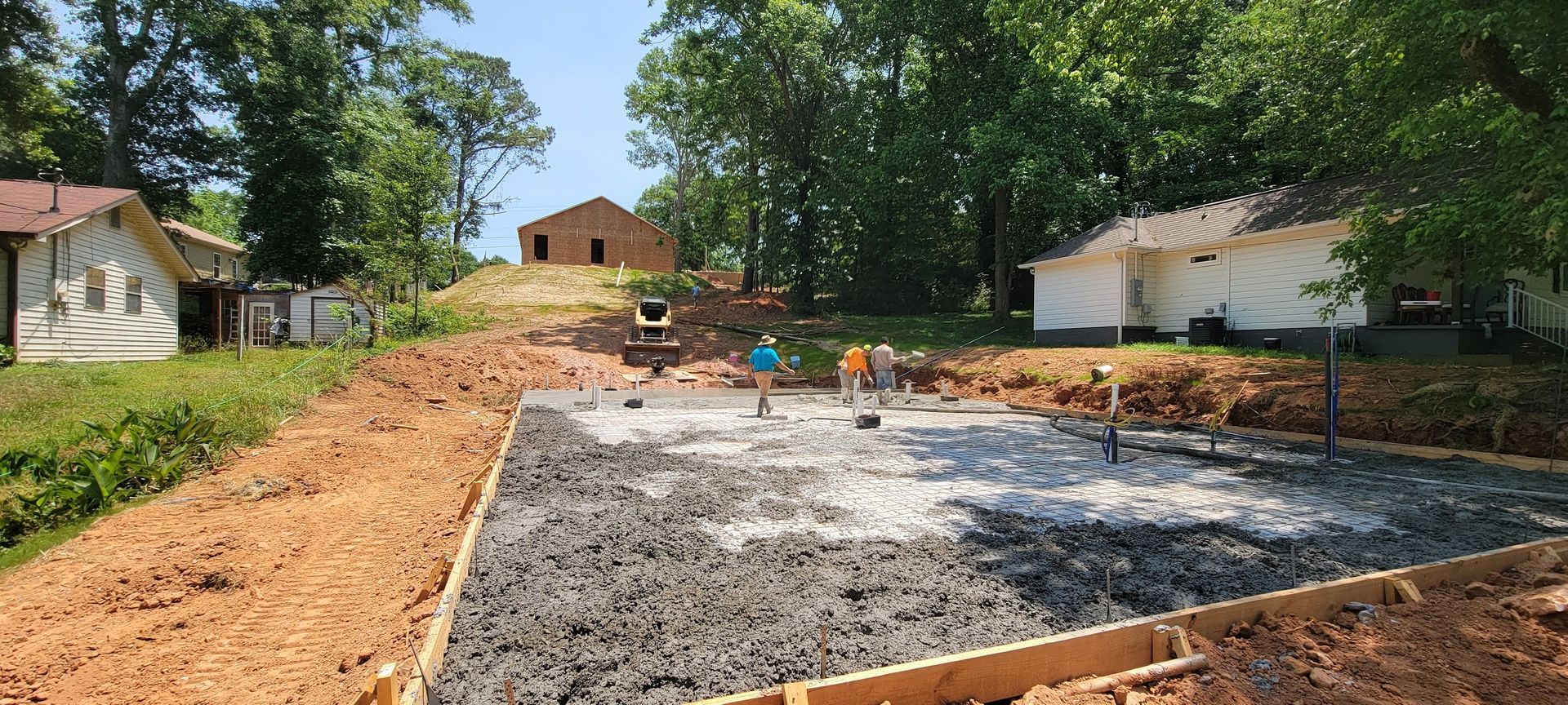 Construction site with concrete foundation and workers in a tree-lined yard