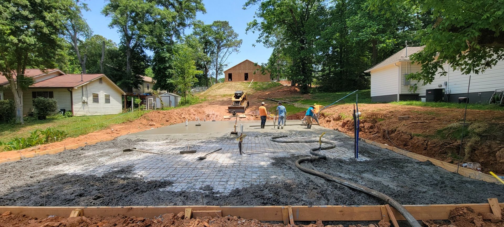 People working on a concrete foundation site between houses and trees