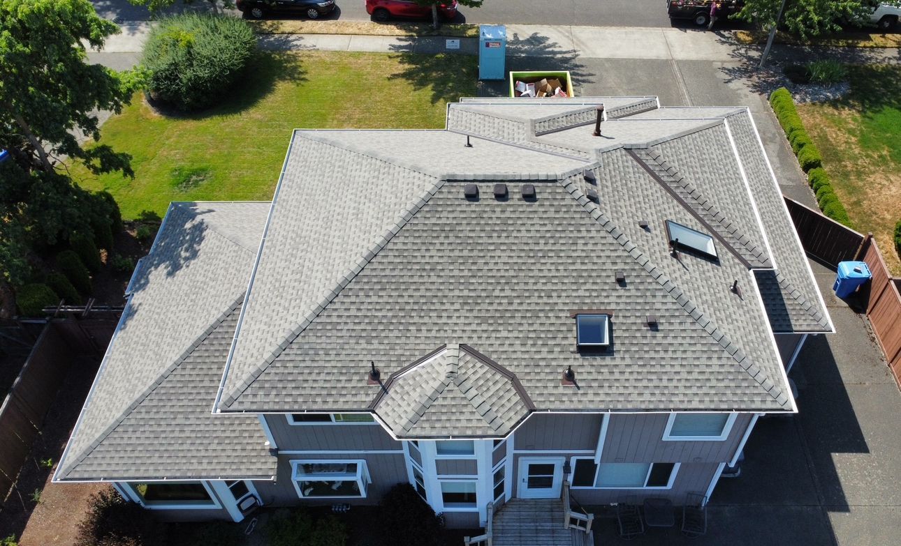 Aerial view of a house with a gray shingled roof and surrounding yard