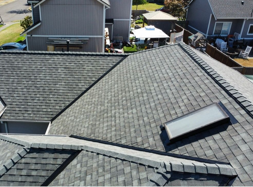 Rooftop with gray shingles and a skylight, viewed from above in a residential neighborhood.