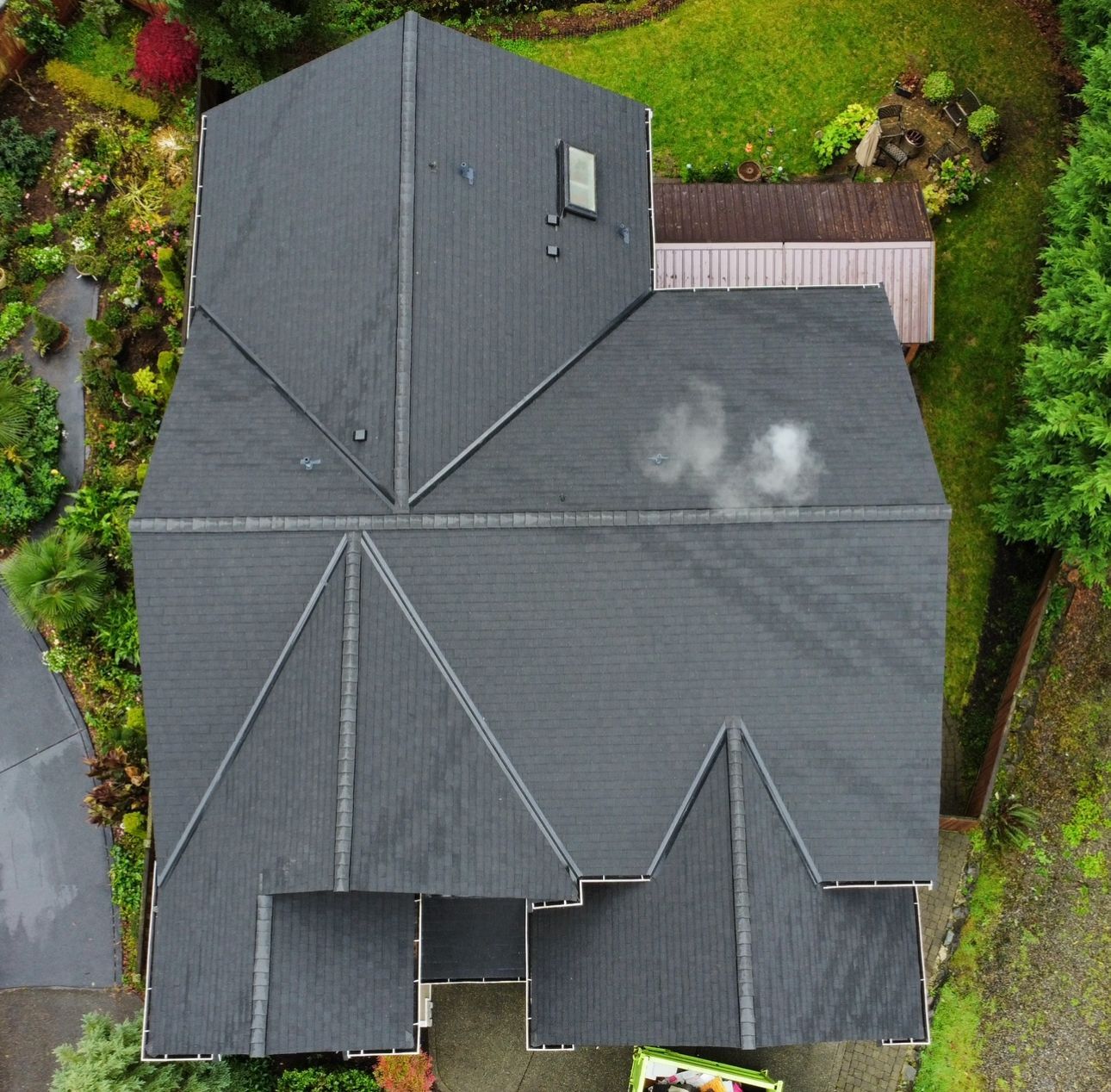 Aerial view of a dark gray house roof surrounded by green trees and shrubs.
