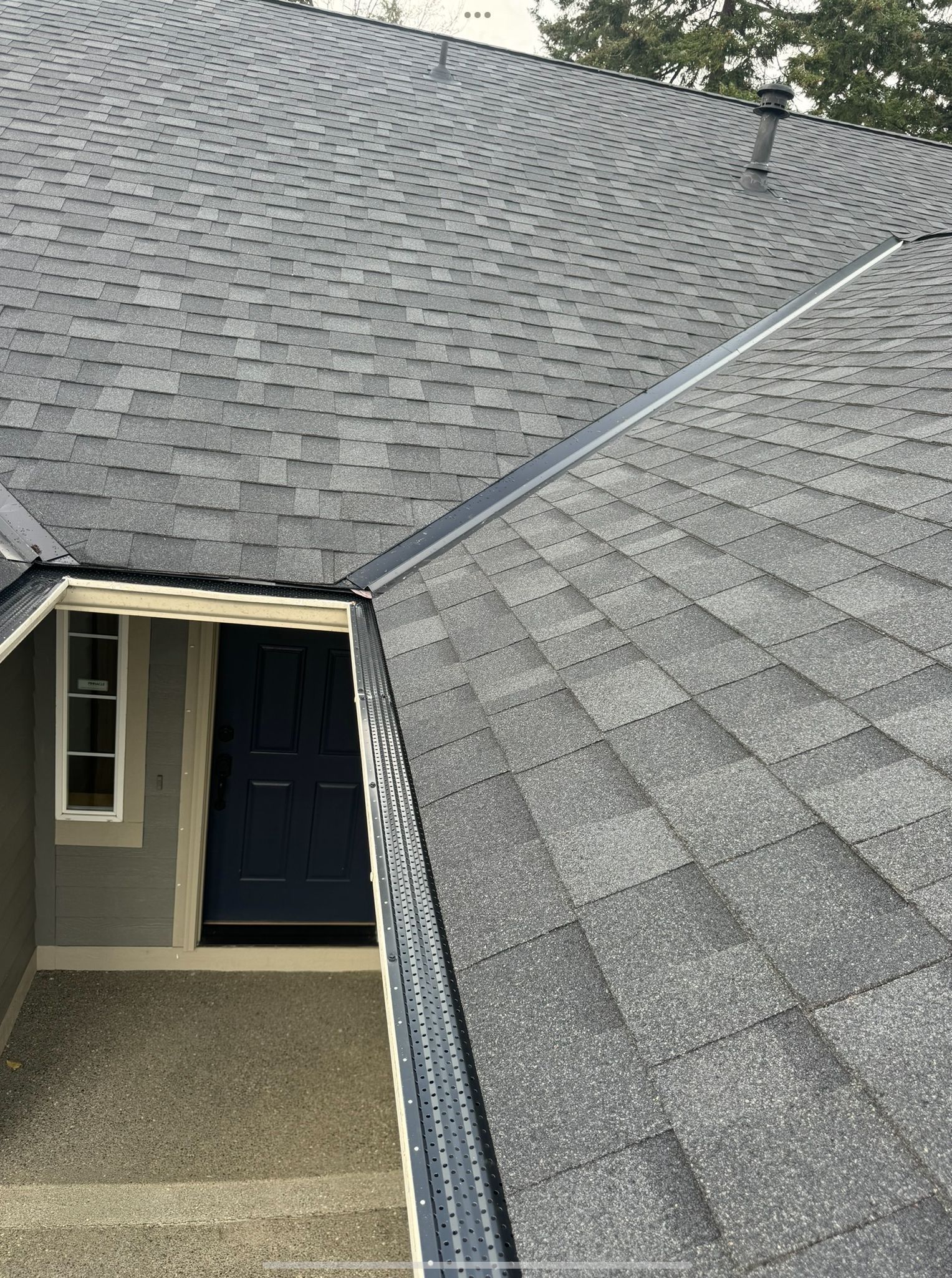Residential roof with gray shingles and a visible roof valley above a covered entryway
