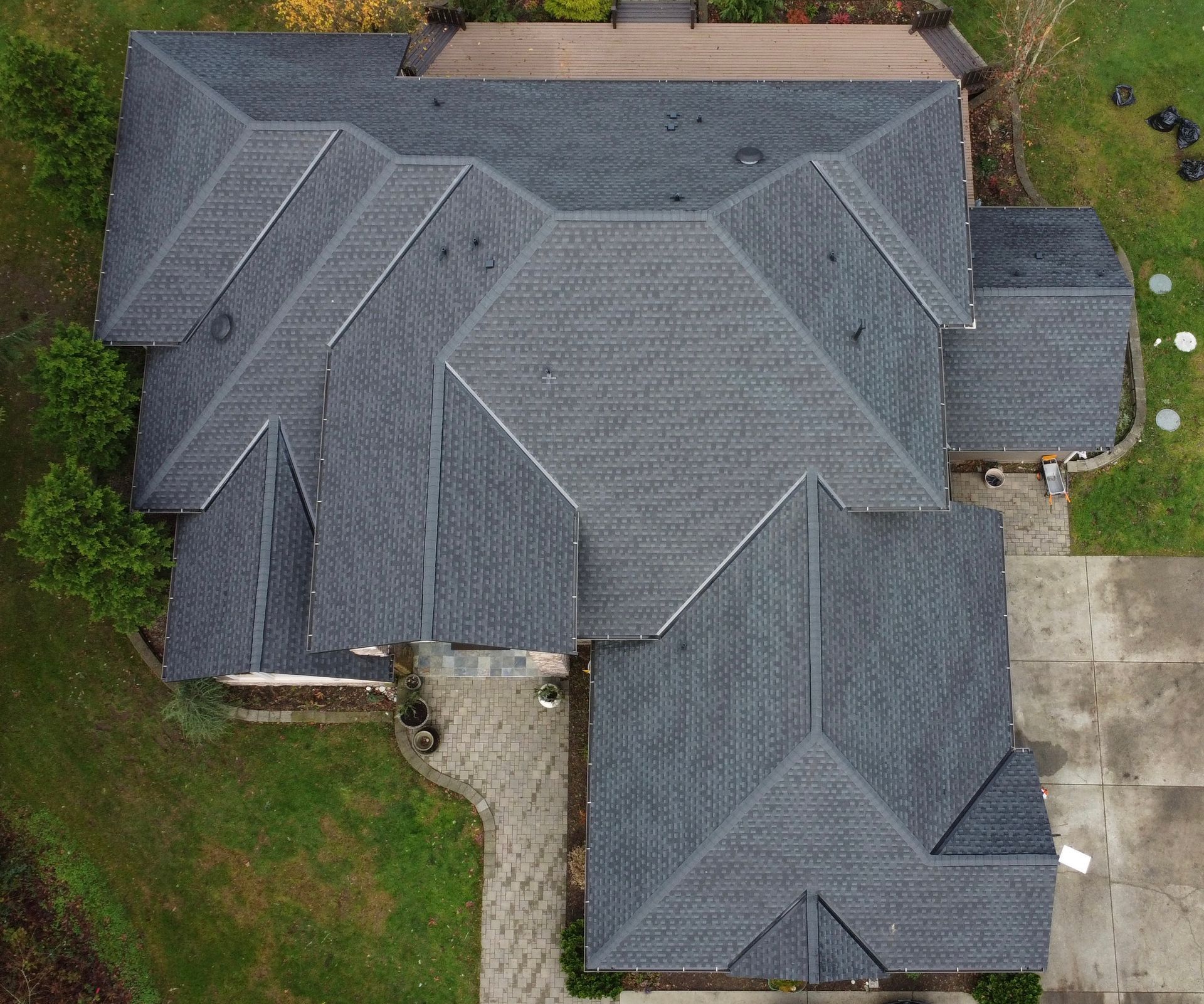 Aerial view of a gray shingled house roof with multiple gables and surrounding yard