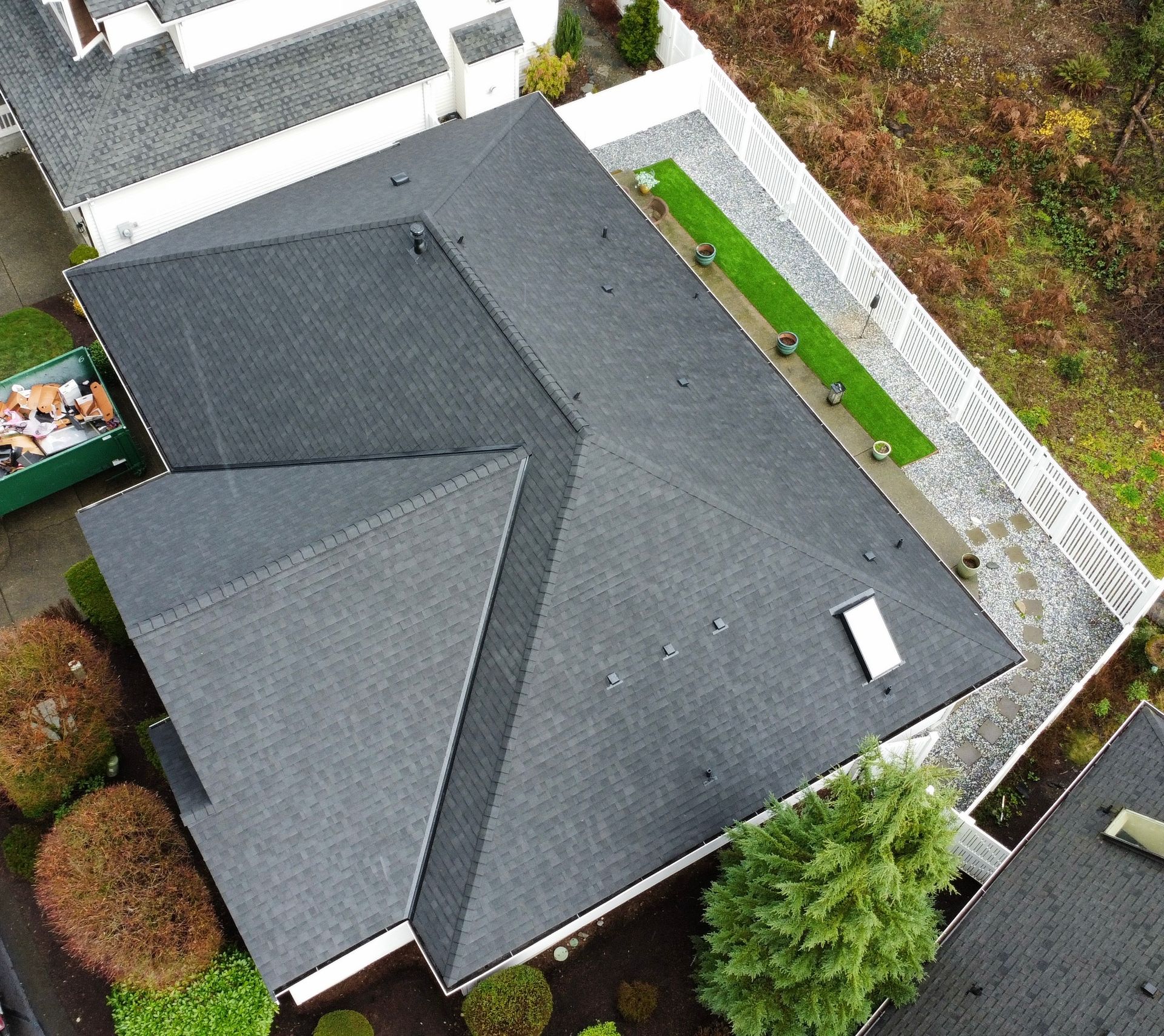 Aerial view of a gray-roofed house with a fenced yard and surrounding trees.