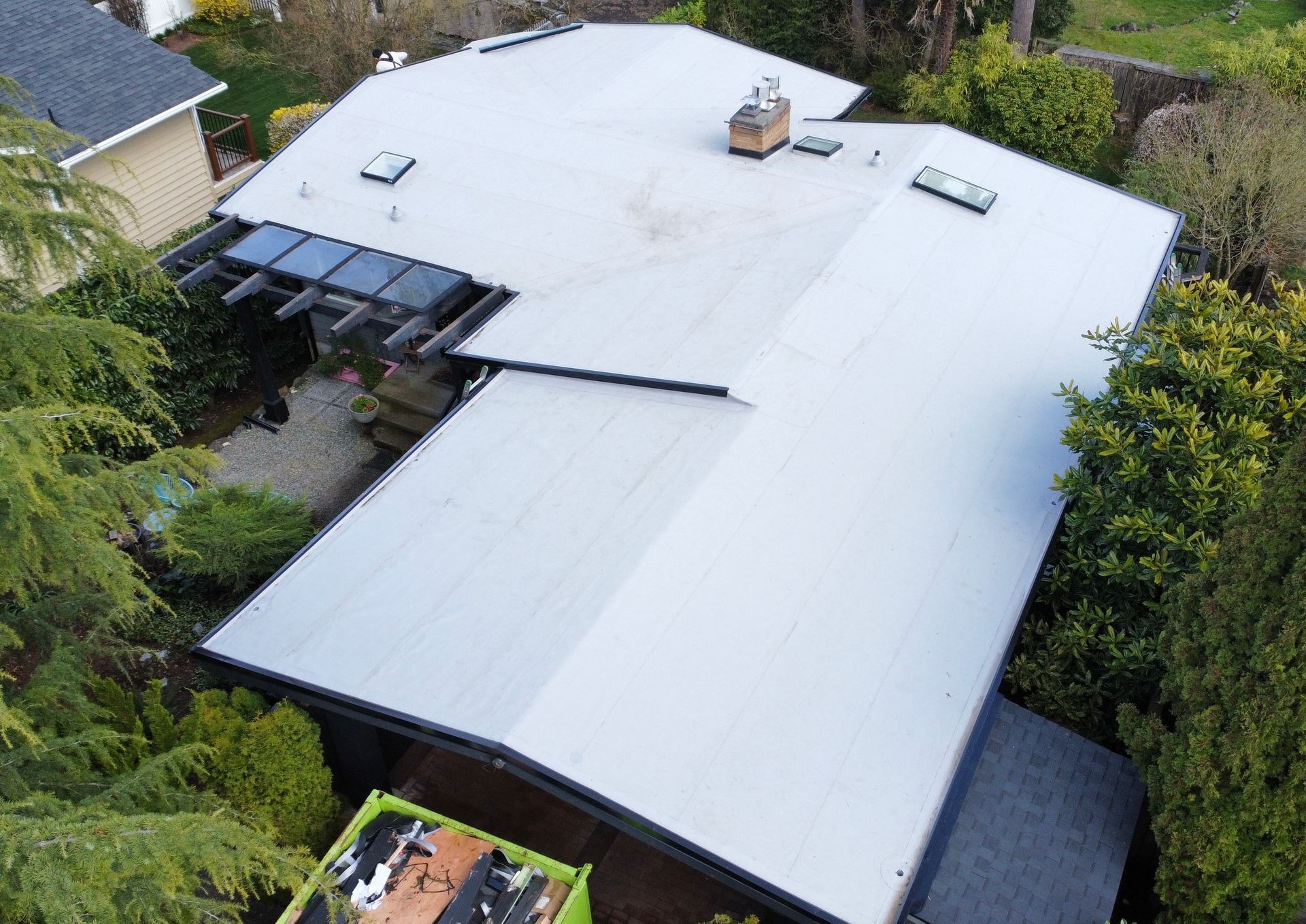 Aerial view of a house with a white roof surrounded by dense greenery.