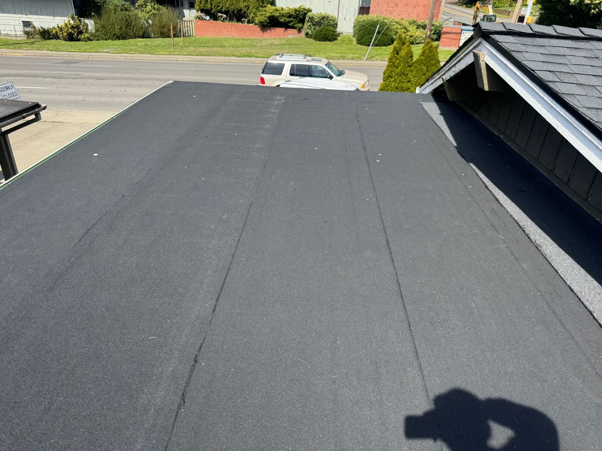 Flat black roof with a shadow, seen from above near a street and parked car.