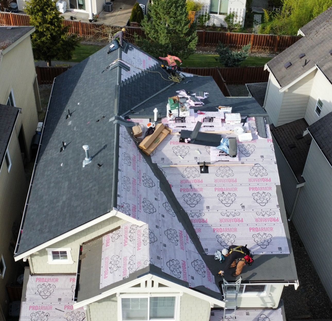 Aerial view of a house roof under repair, with workers and roofing materials on the shingles.