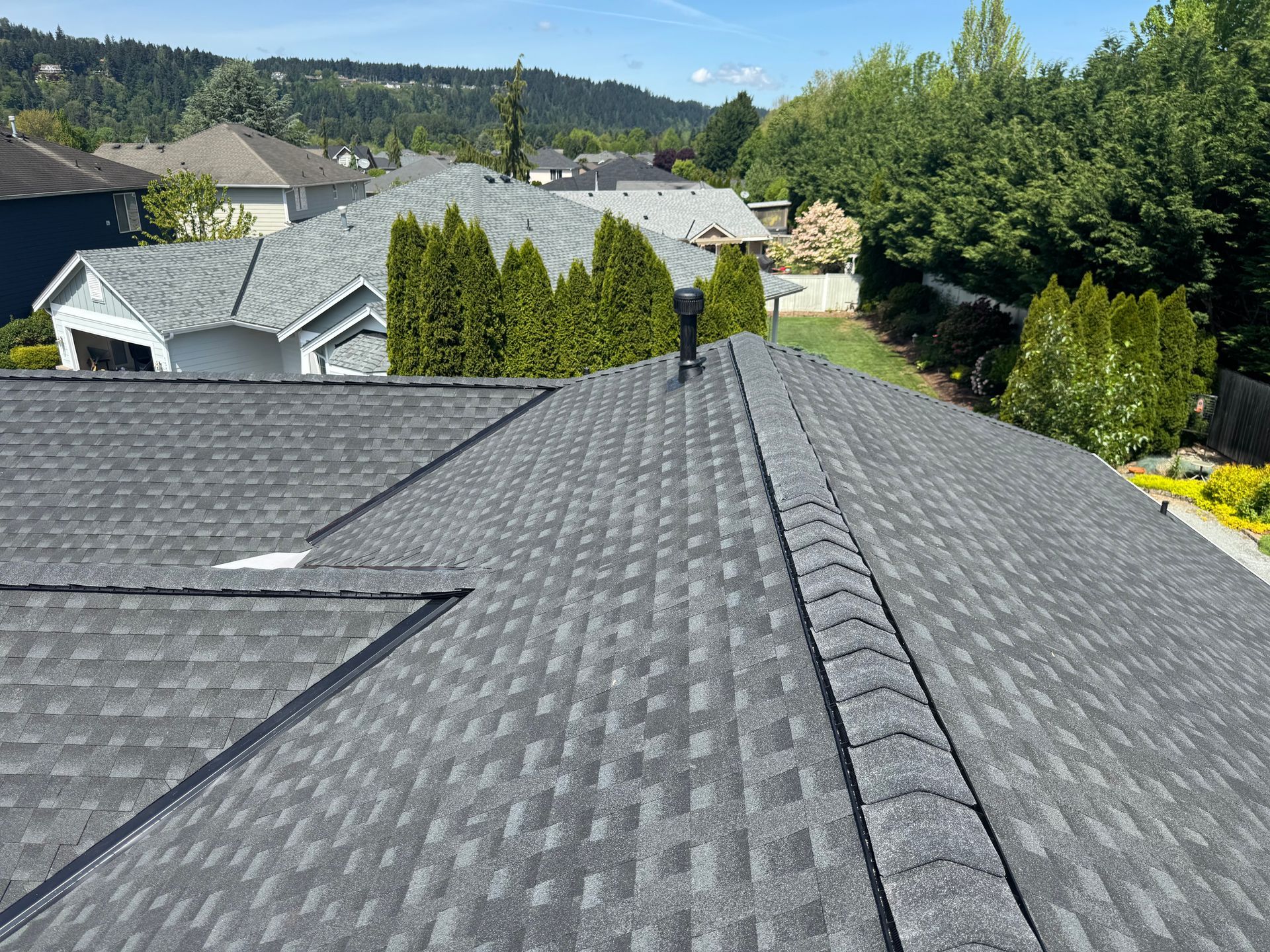View from a shingled rooftop over suburban homes and trees on a sunny day
