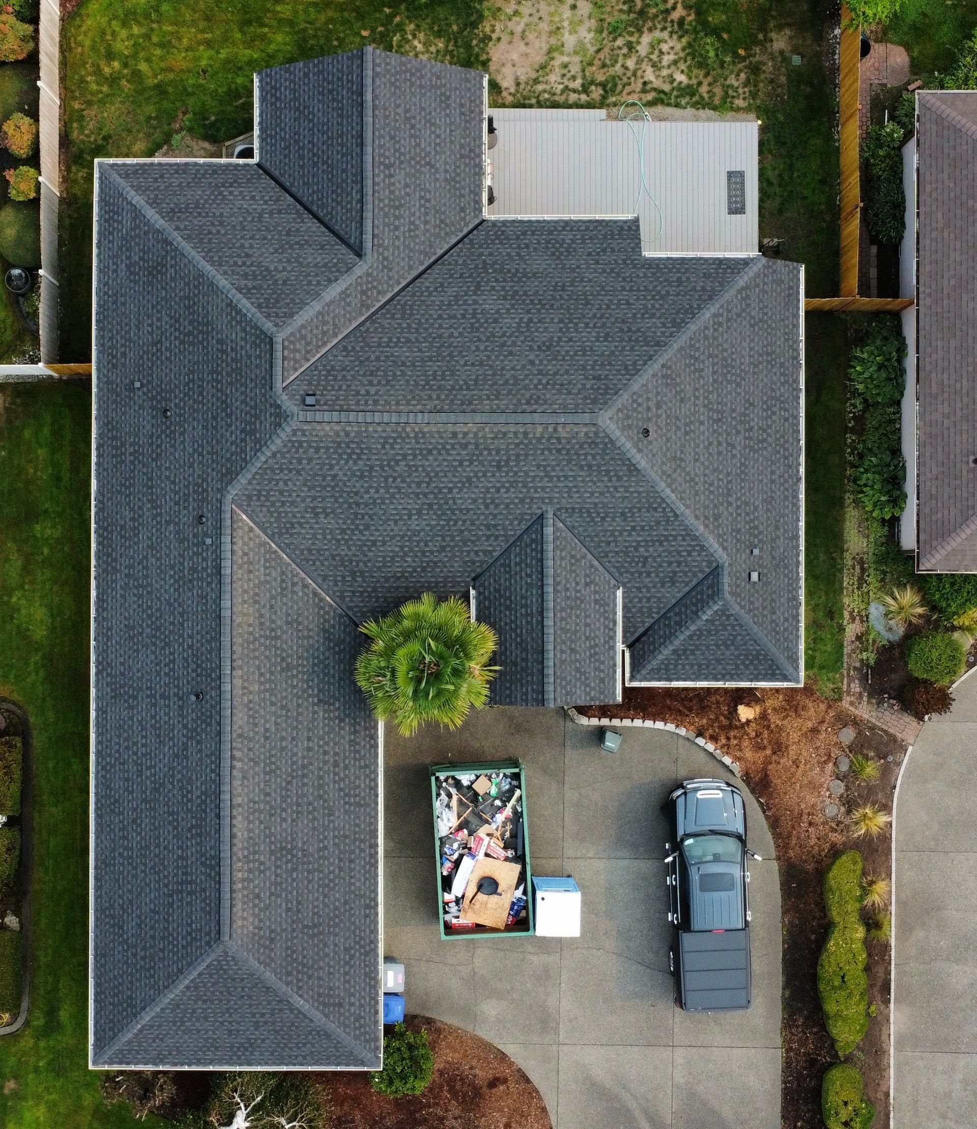 Aerial view of a gray-roofed house with driveway, parked car, and yard work materials.