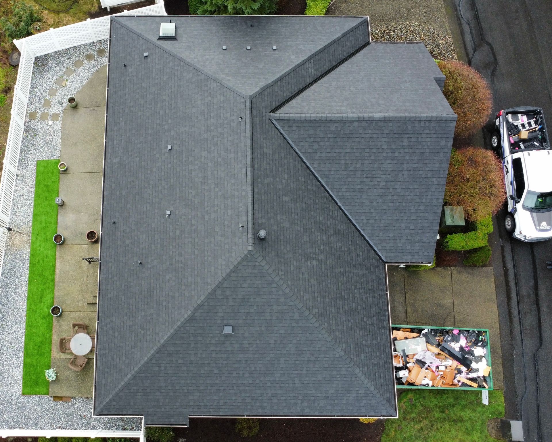Aerial view of a gray-roofed house with a driveway, yard, and parked vehicle beside it.
