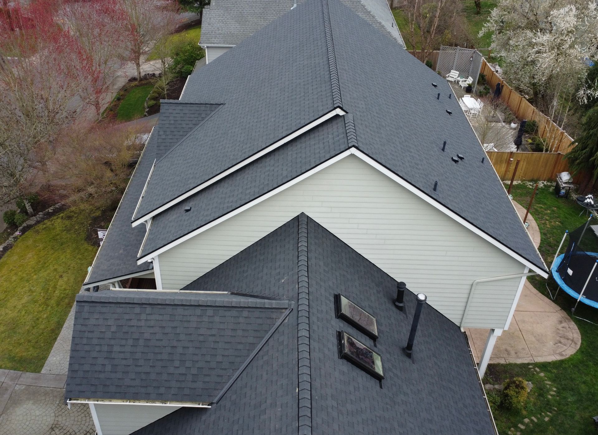 Aerial view of a gray roof with skylights and a chimney on a house surrounded by trees.