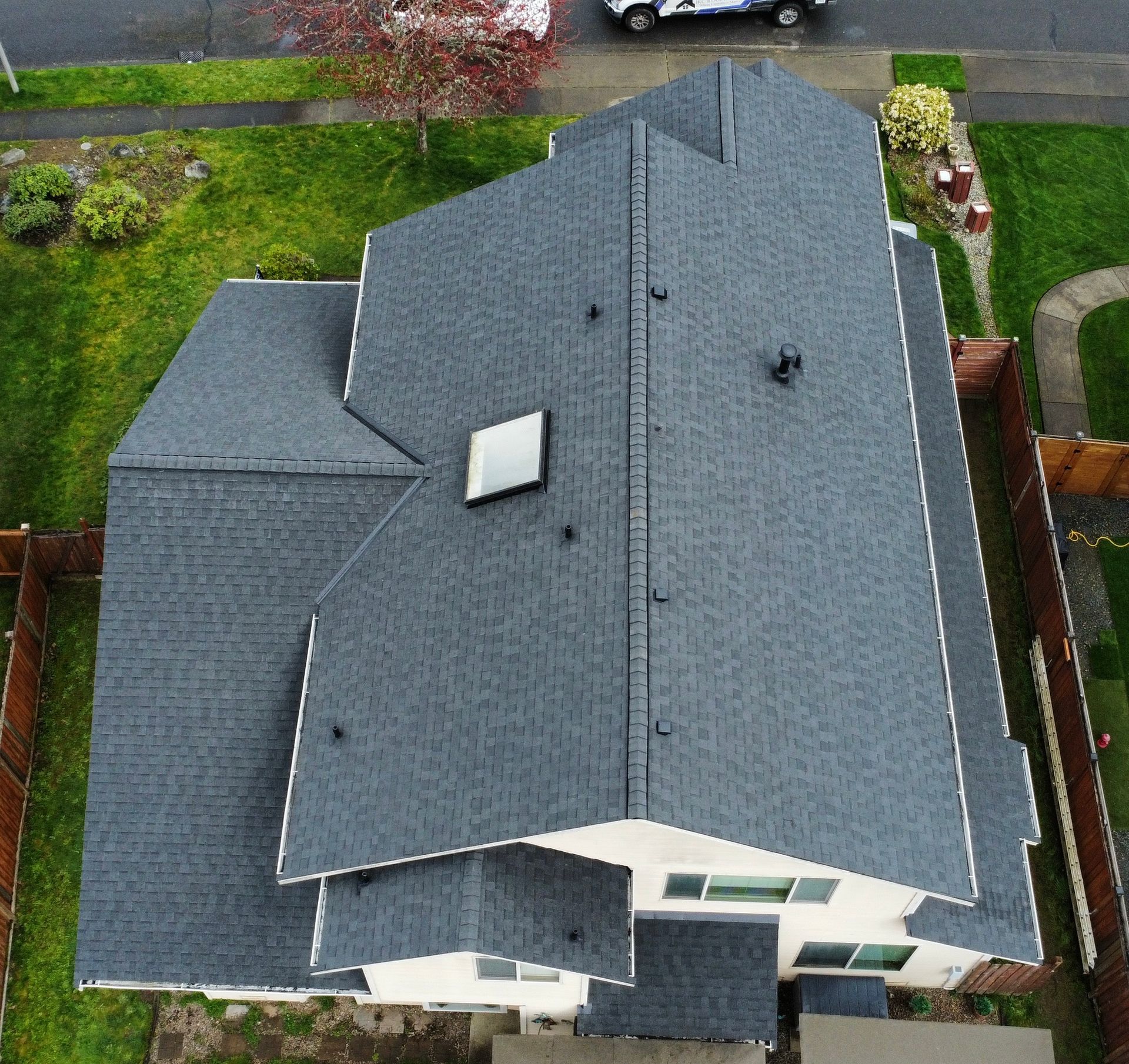 Aerial view of a gray-shingled house with a small skylight and green yard around it
