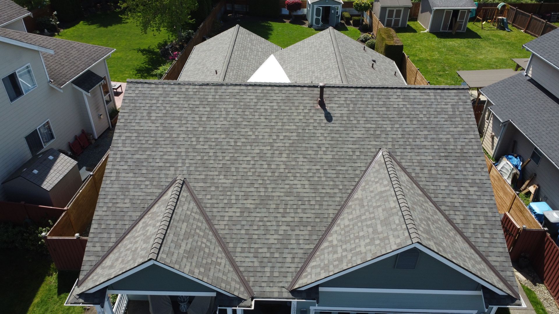 Aerial view of a gray shingled suburban house roof with dormers and neighboring homes