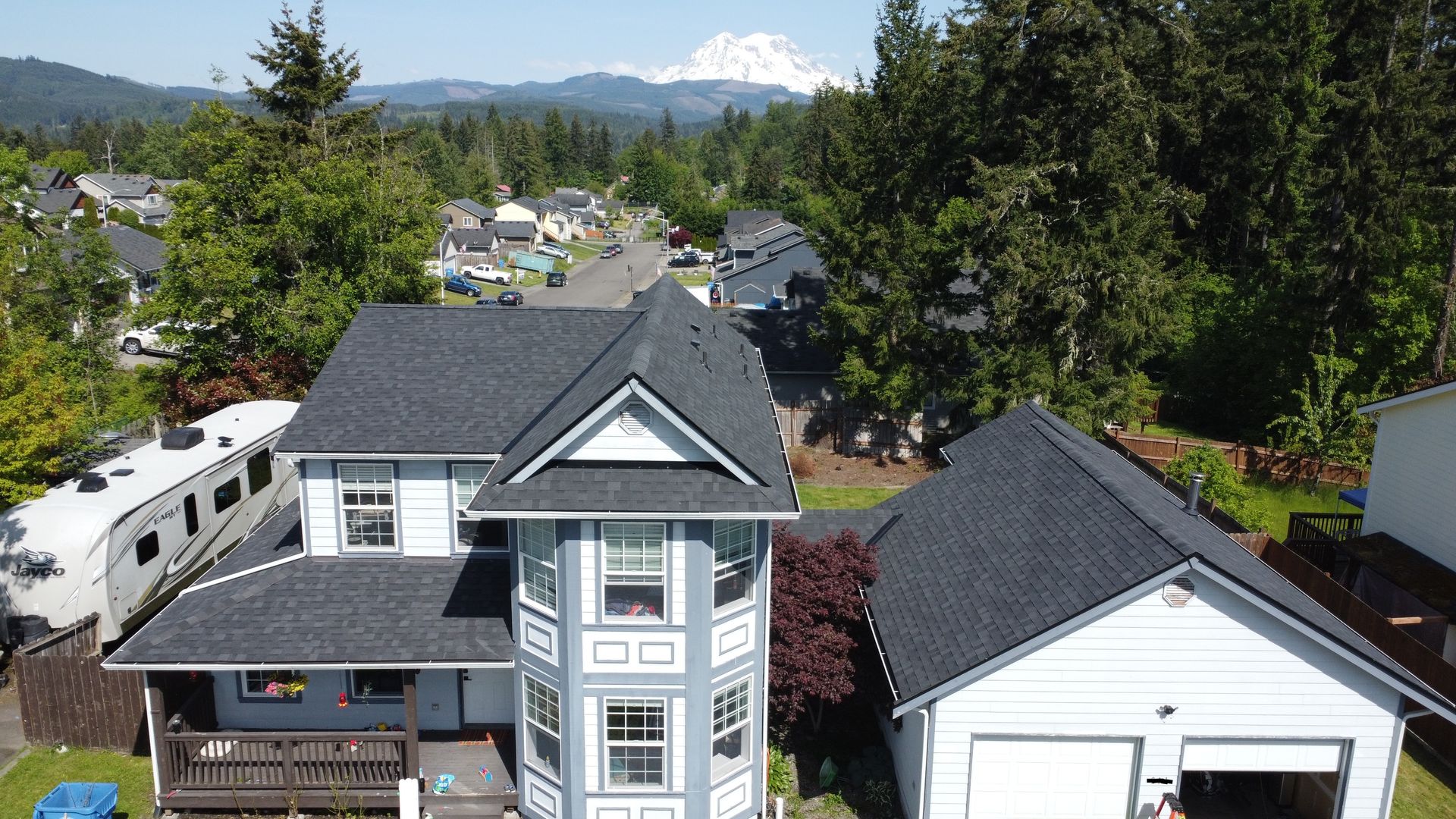 Aerial view of houses in a tree-lined neighborhood with mountains in the distance and a snow-capped peak.