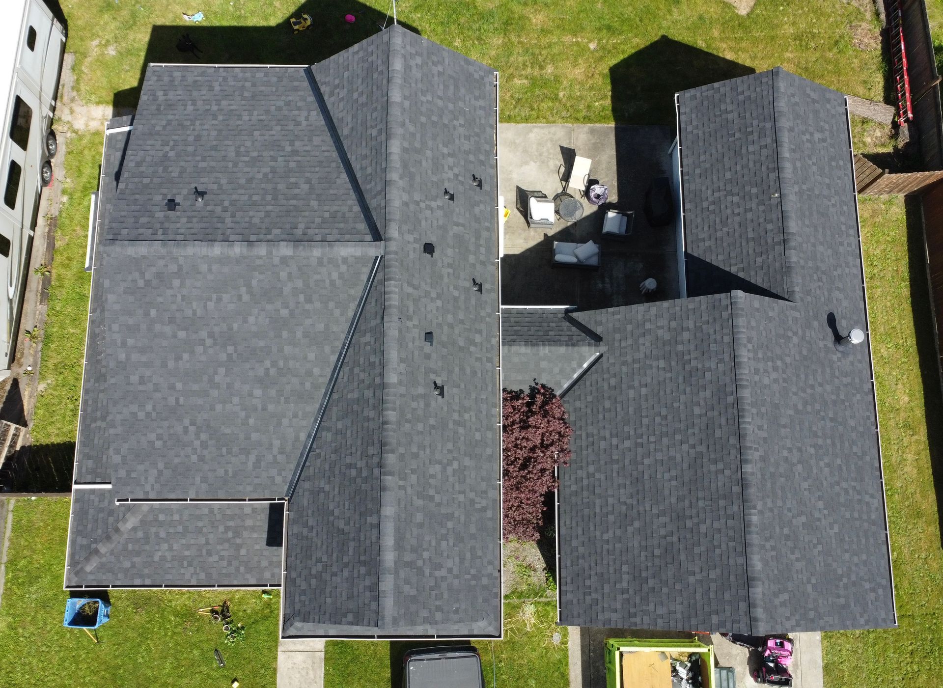 Aerial view of two gray-roofed houses with a small backyard patio between them.