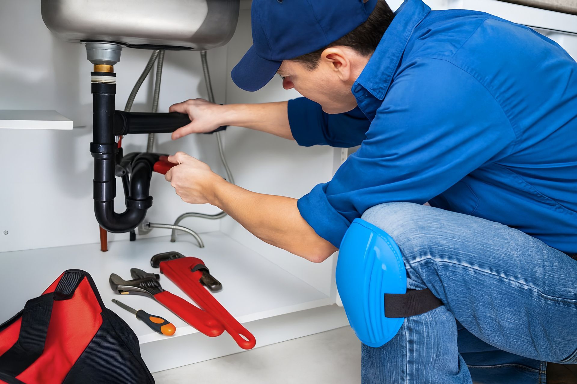 Plumber repairing pipes under a sink with tools laid out on the floor.