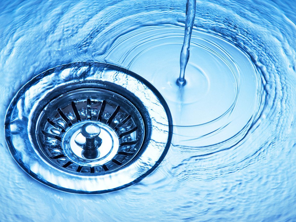 Water flowing into a stainless steel sink drain, creating ripples.