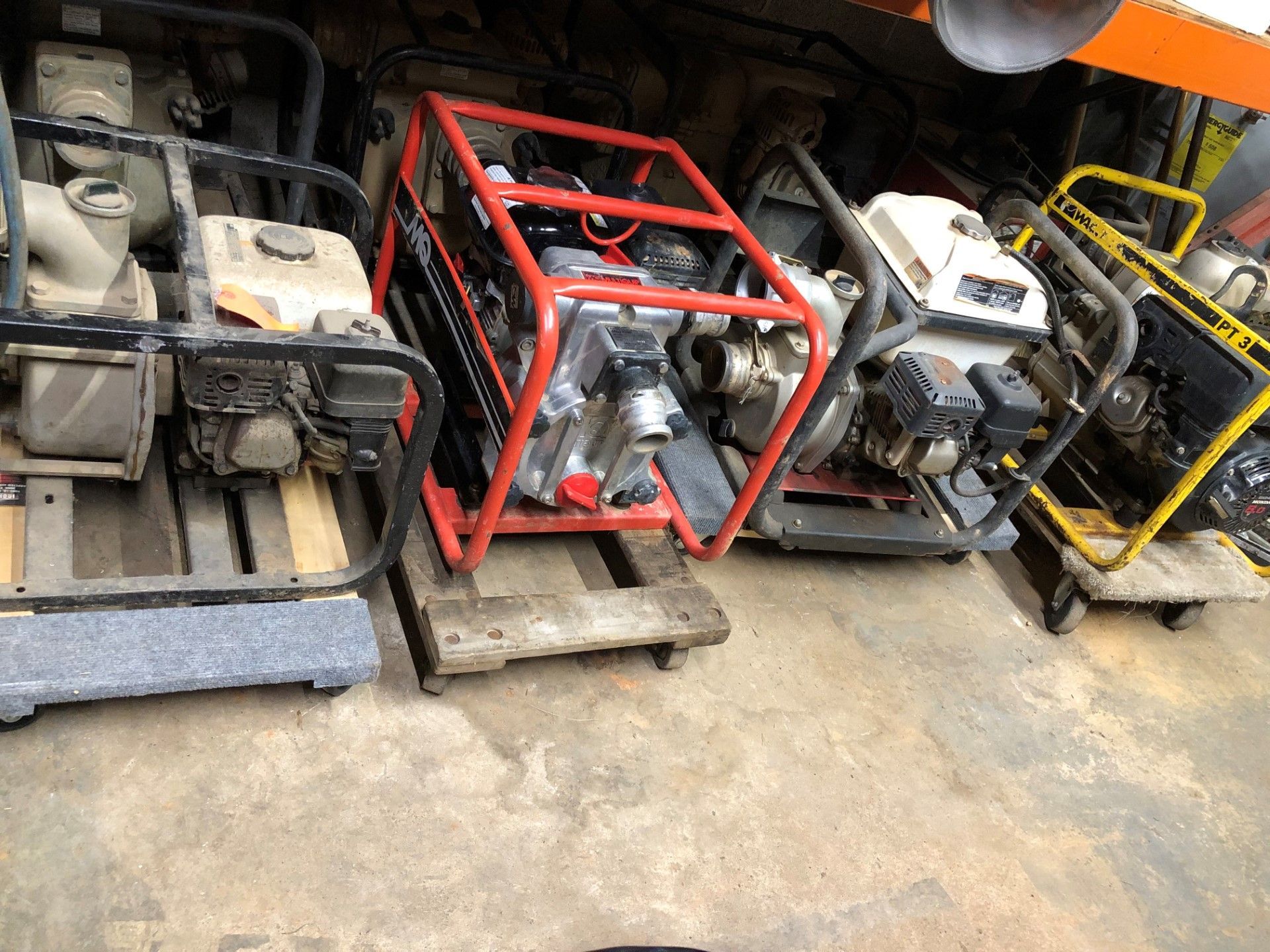 Several water pumps in different colors and frames, sitting on pallets.