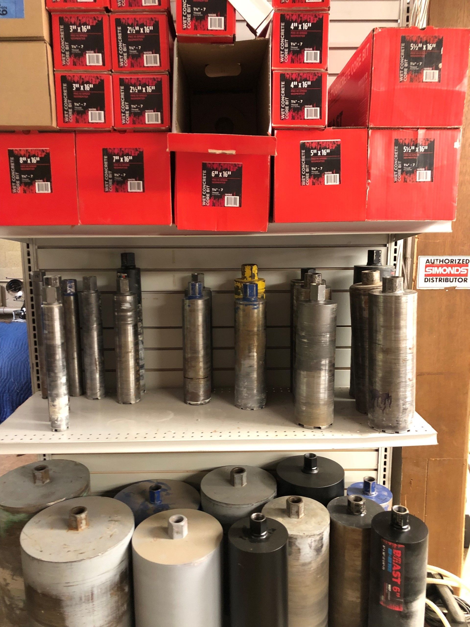 Shelf display of cylindrical concrete core drill bits, with red boxed bits stacked above.