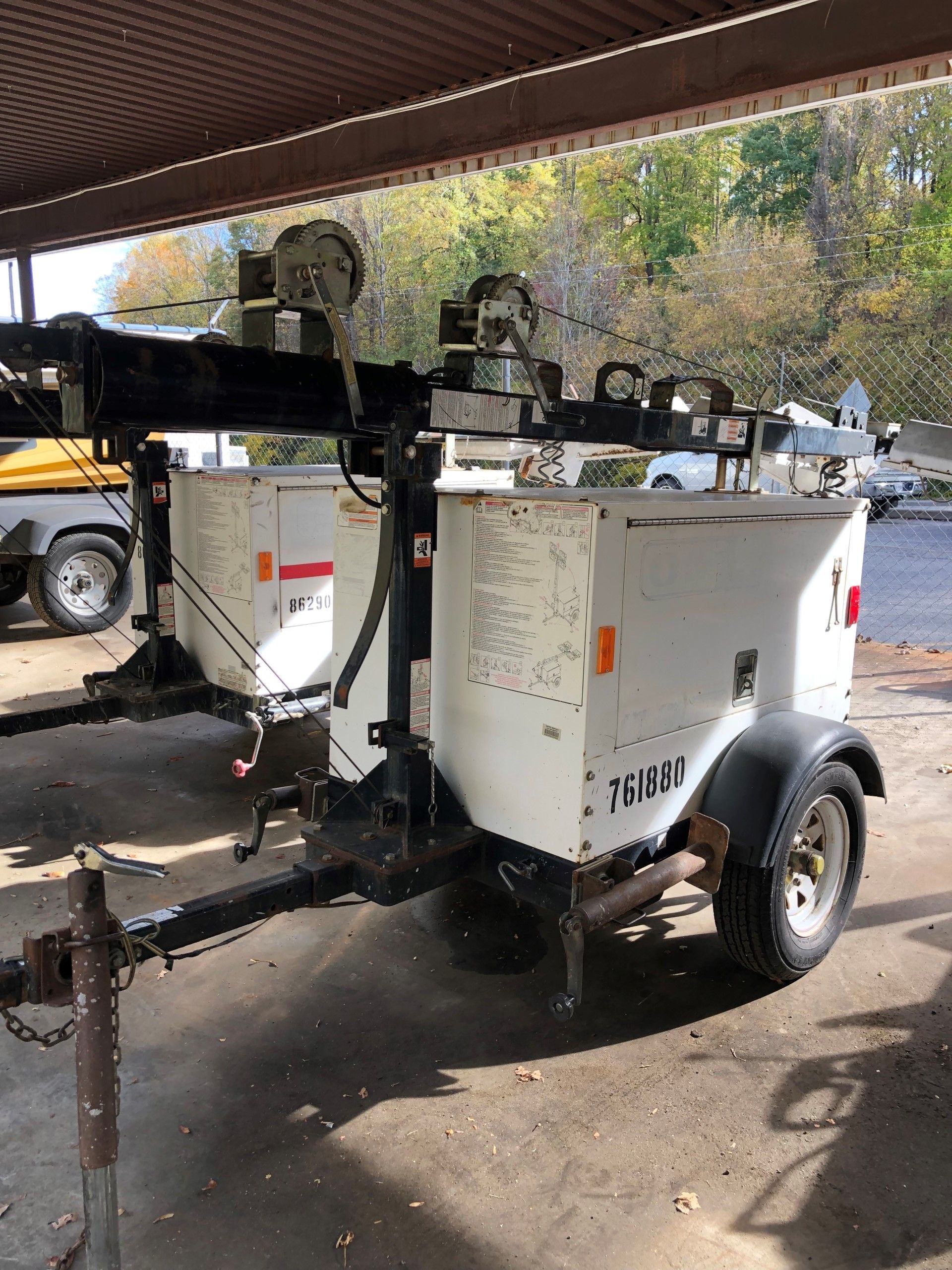 Mobile light tower on a trailer, white cabinets, black frame, under a shelter.