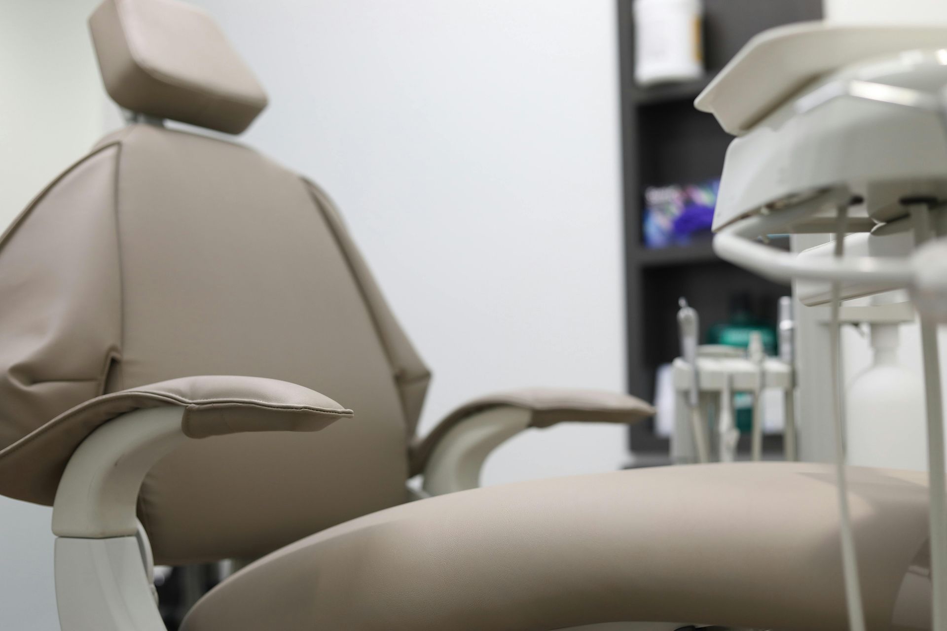 Beige dental chair with armrests, near dental tools and shelf in an office.