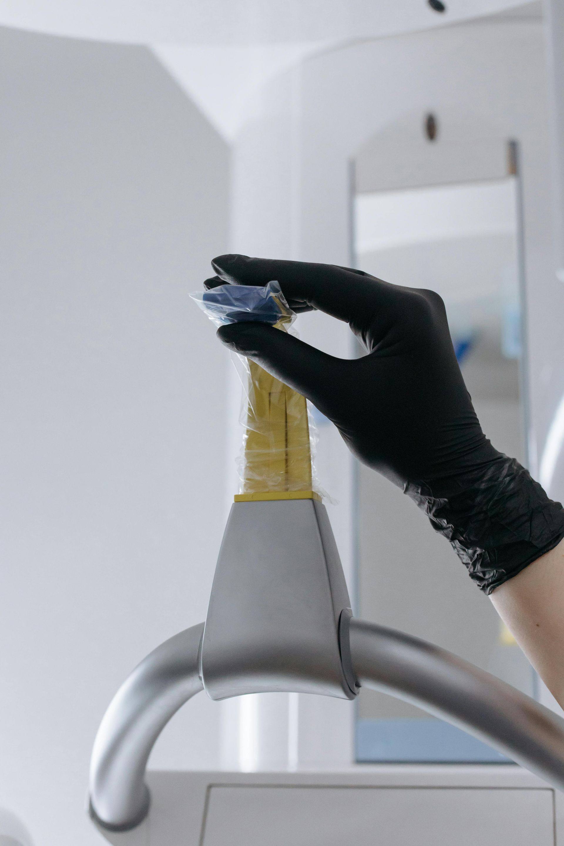 Hand in black glove holding blue dental tool above a yellow-taped part of a dental machine.