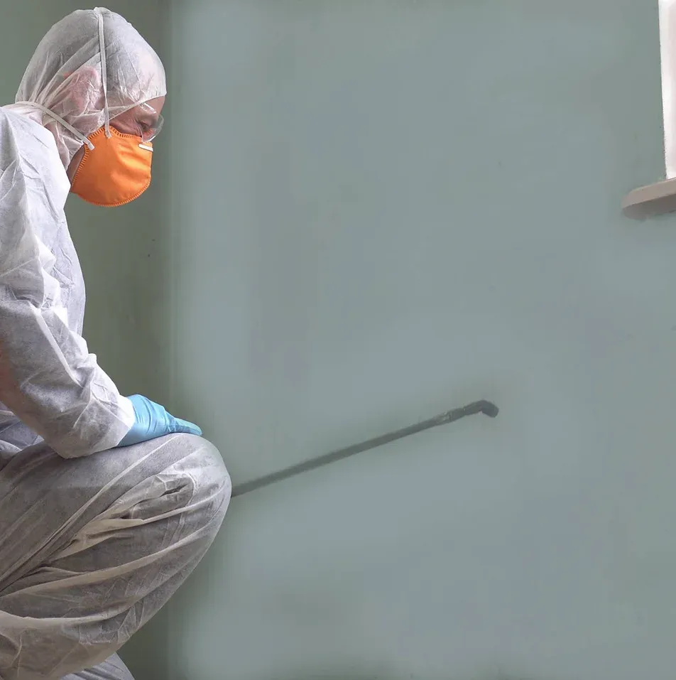 A person wearing a mask and gloves is squatting down in a room.