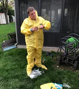 A man in a yellow protective suit is standing in the grass.